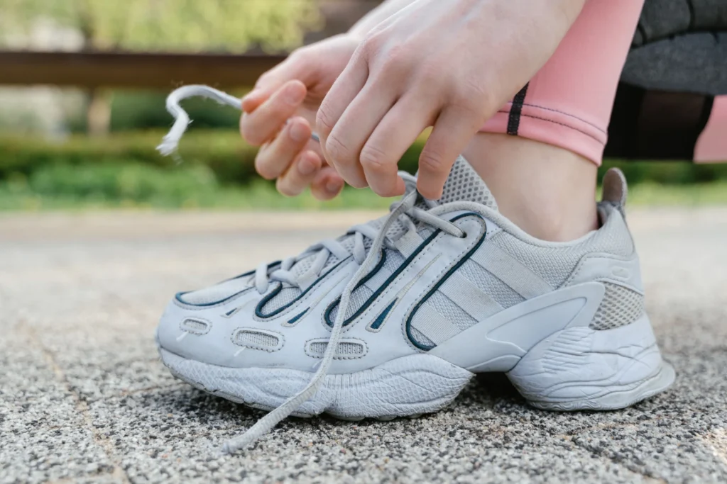 Zbliżenie na kobietę wiążącą białe sznurowadła w białych sneakersach podczas ćwiczeń na zewnątrz.