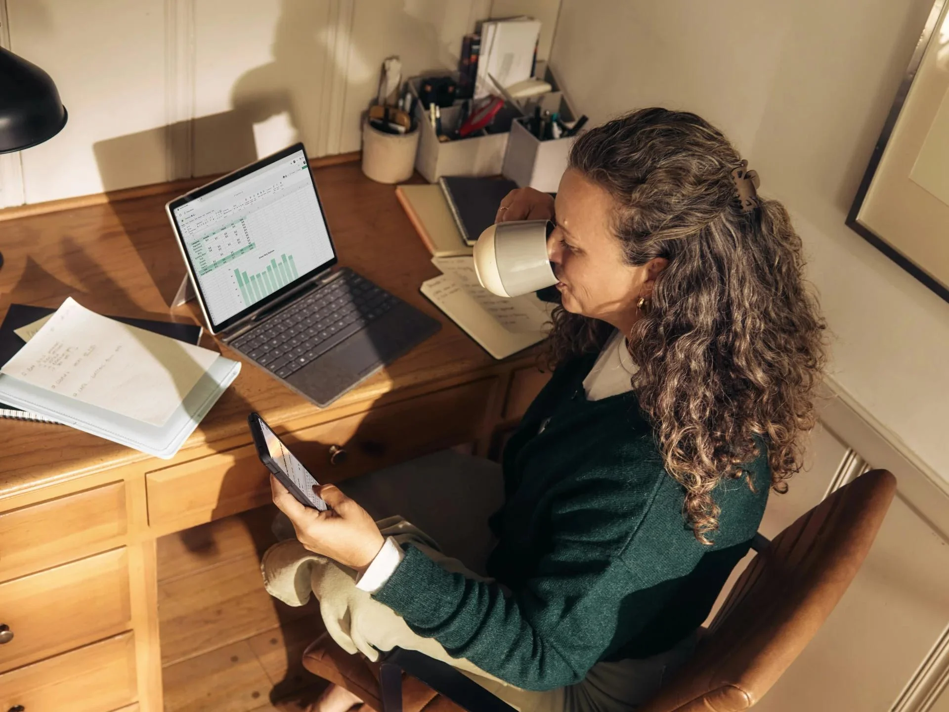 Kobieta pracuje przy biurku, używając laptopa i tabletu, skupiona na zadaniach.